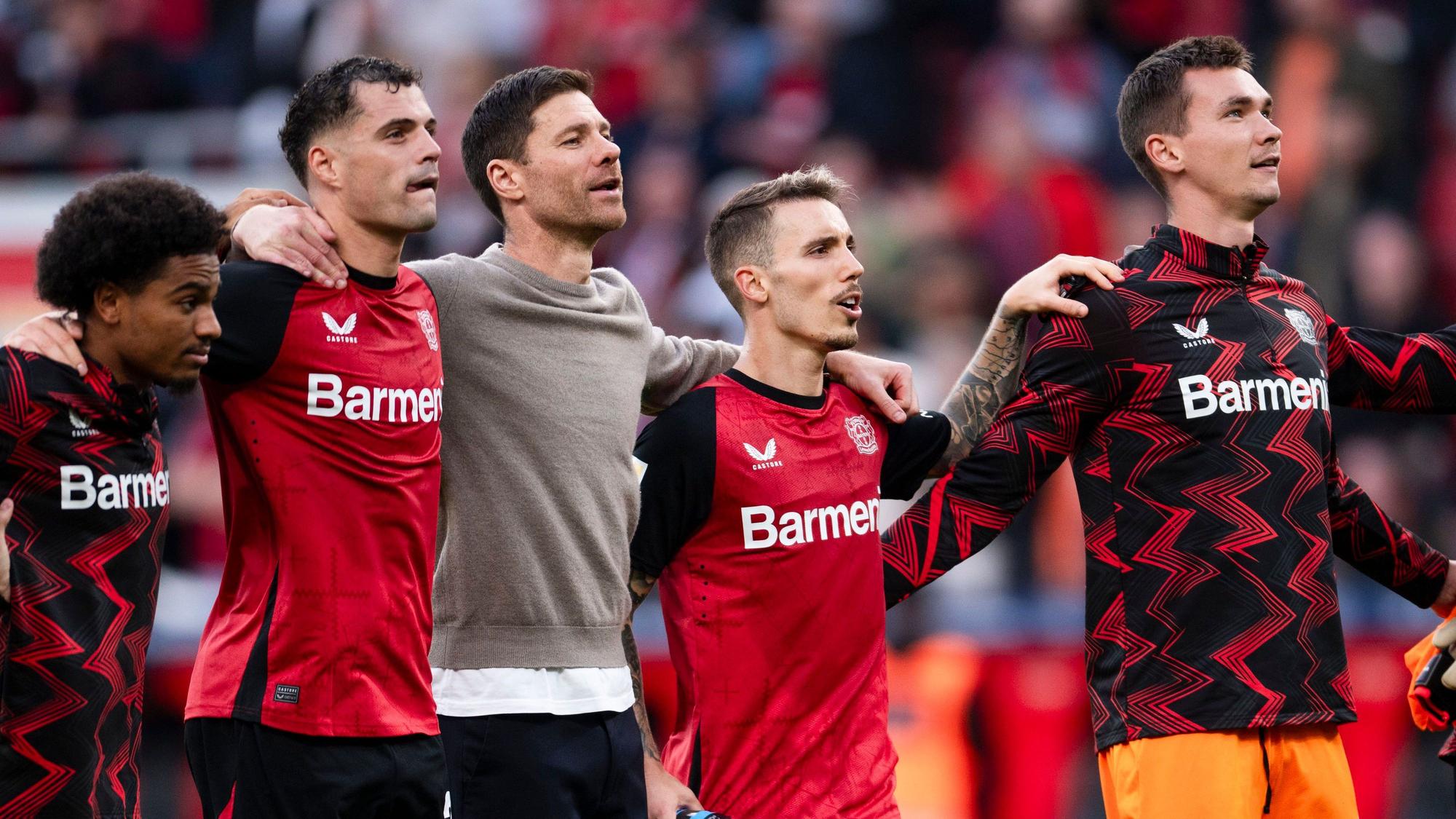 Von links nach rechts: Leverkusens Amine Adli, Granit Xhaka, Trainer Xabi Alonso, Alejandro Grimaldo und Matej Kovar feiern nach der Partie vor der Fankurve.