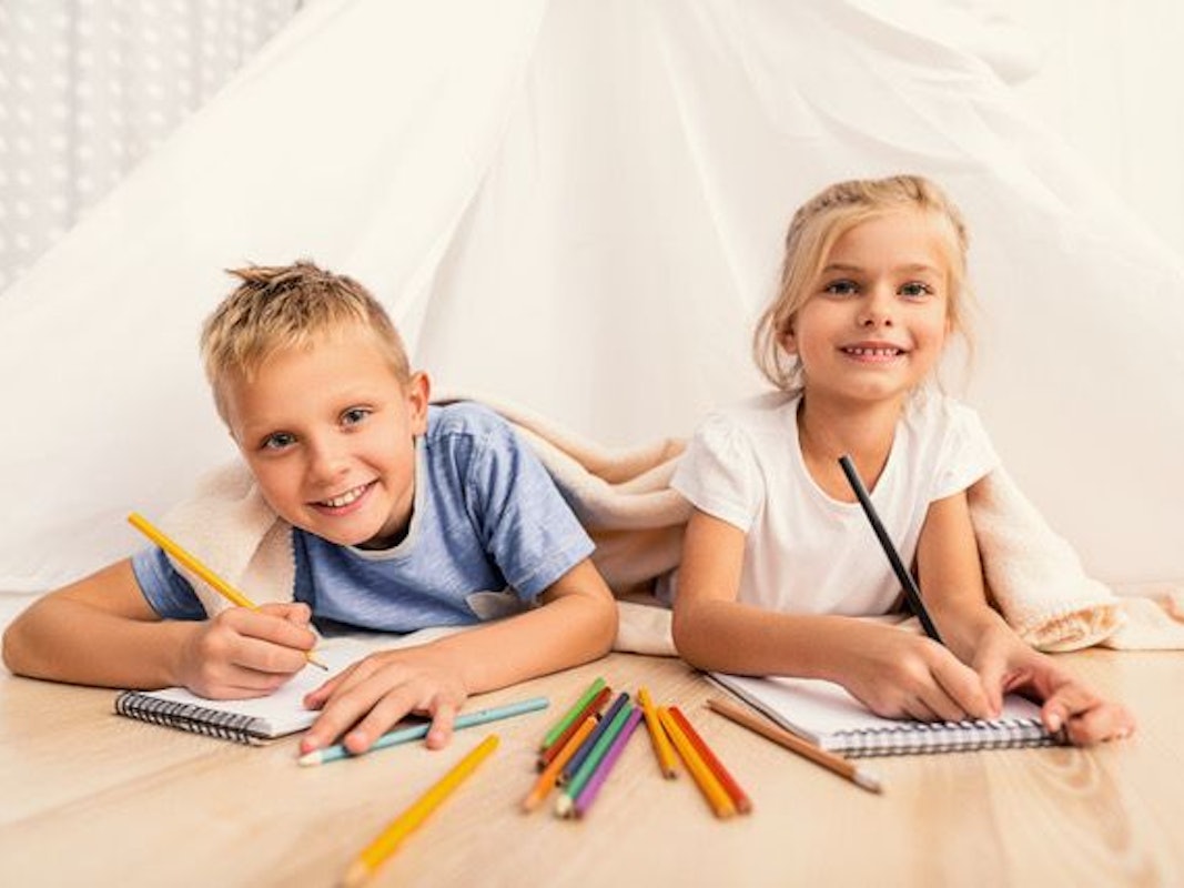 Zwei Kinder liegen auf dem Boden und haben Buntstifte in der Hand.