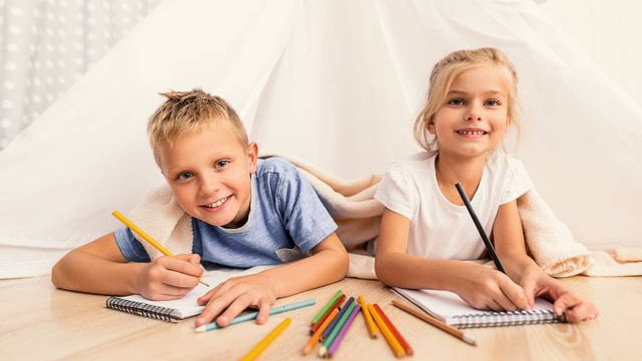 Zwei Kinder liegen auf dem Boden und haben Buntstifte in der Hand.