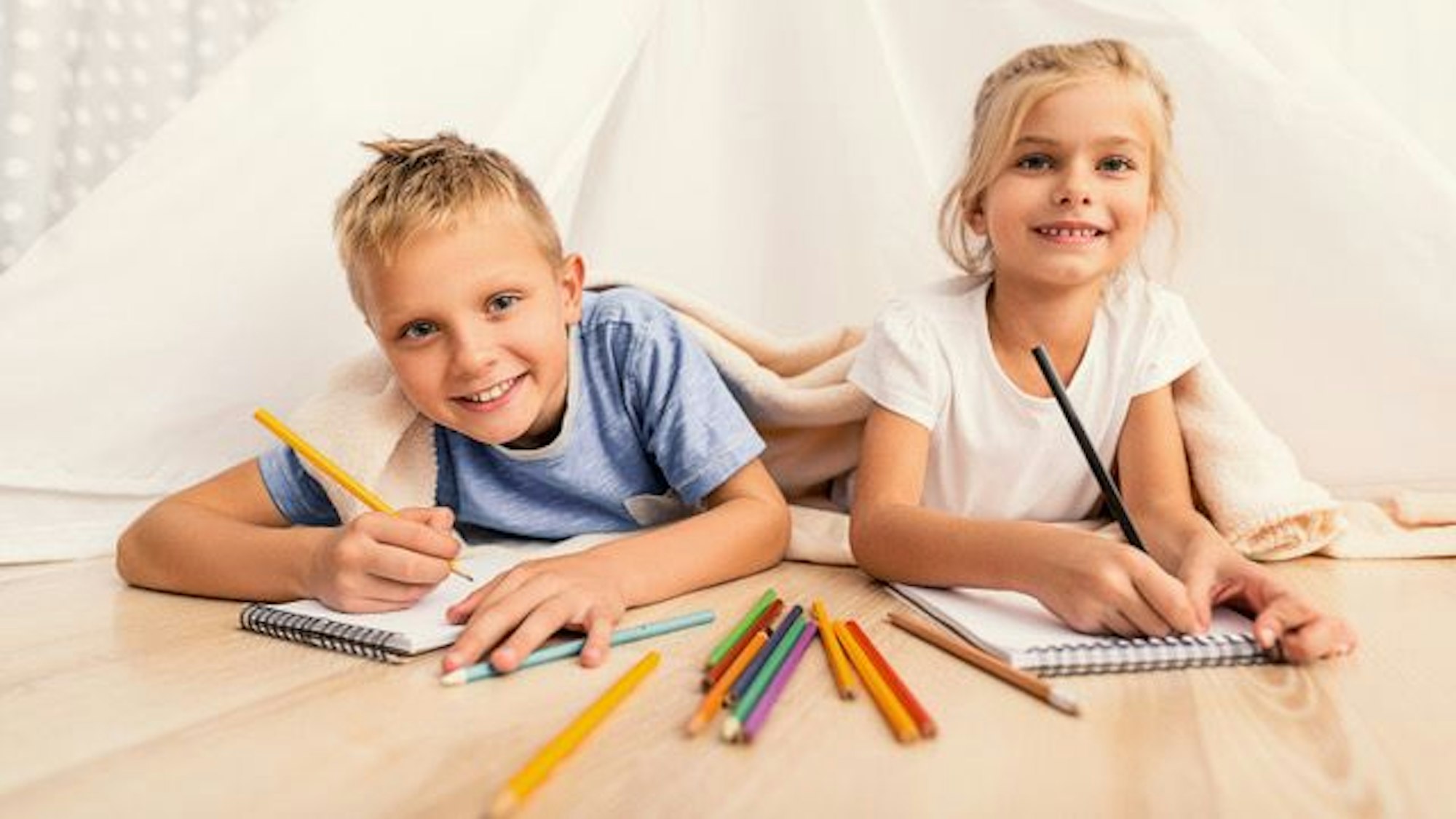 Zwei Kinder liegen auf dem Boden und haben Buntstifte in der Hand.