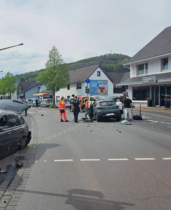An einer Kreuzung stehen zwei verunglückte Fahrzeuge, auf der Fahrbahn Trümmerteile. Einsatzkräfte von Feuerwehr und Rettungsdienst sind im Einsatz.