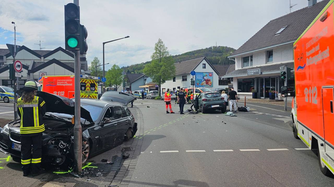 An einer Kreuzung stehen zwei verunglückte Fahrzeuge, auf der Fahrbahn Trümmerteile. Einsatzkräfte von Feuerwehr und Rettungsdienst sind im Einsatz.