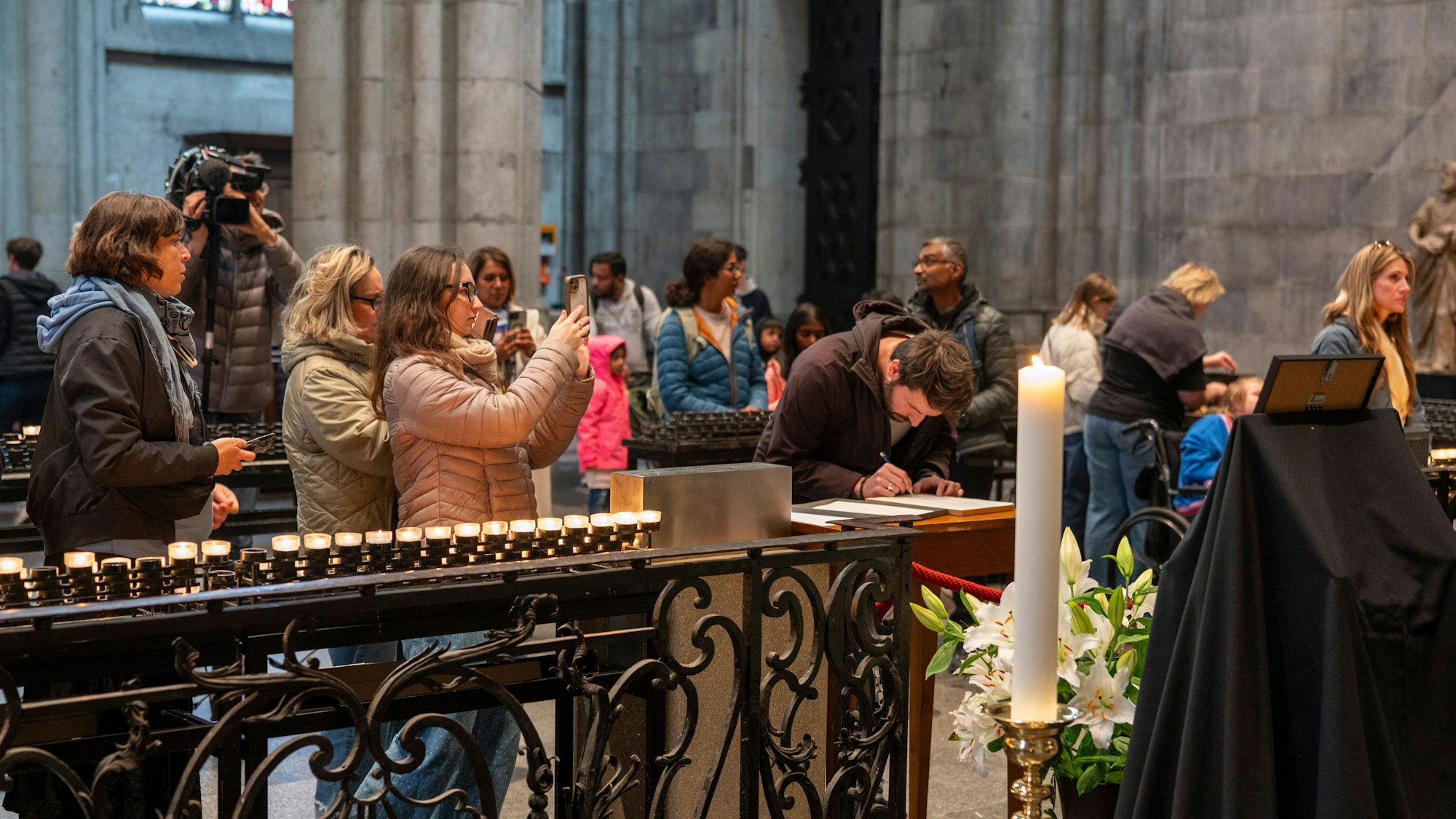 Mehrerer Personen drängen sich im Kölner Dom, ein Mann schreibt in das ausgelegte Kondolenzbuch.