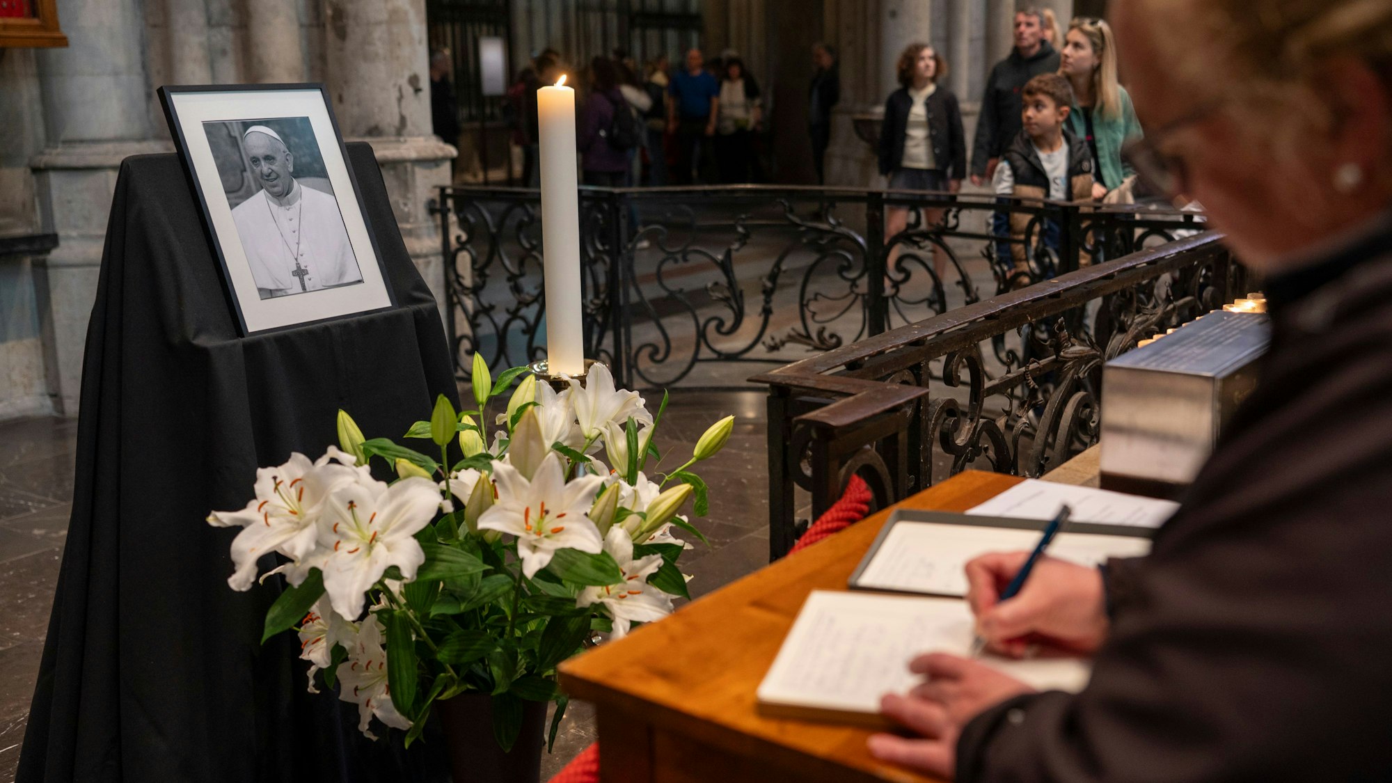 Im Kölner Dom steht ein Foto des verstorbenen Papstes, davor trägt eine Person sich in das Kondolenzbuch ein.