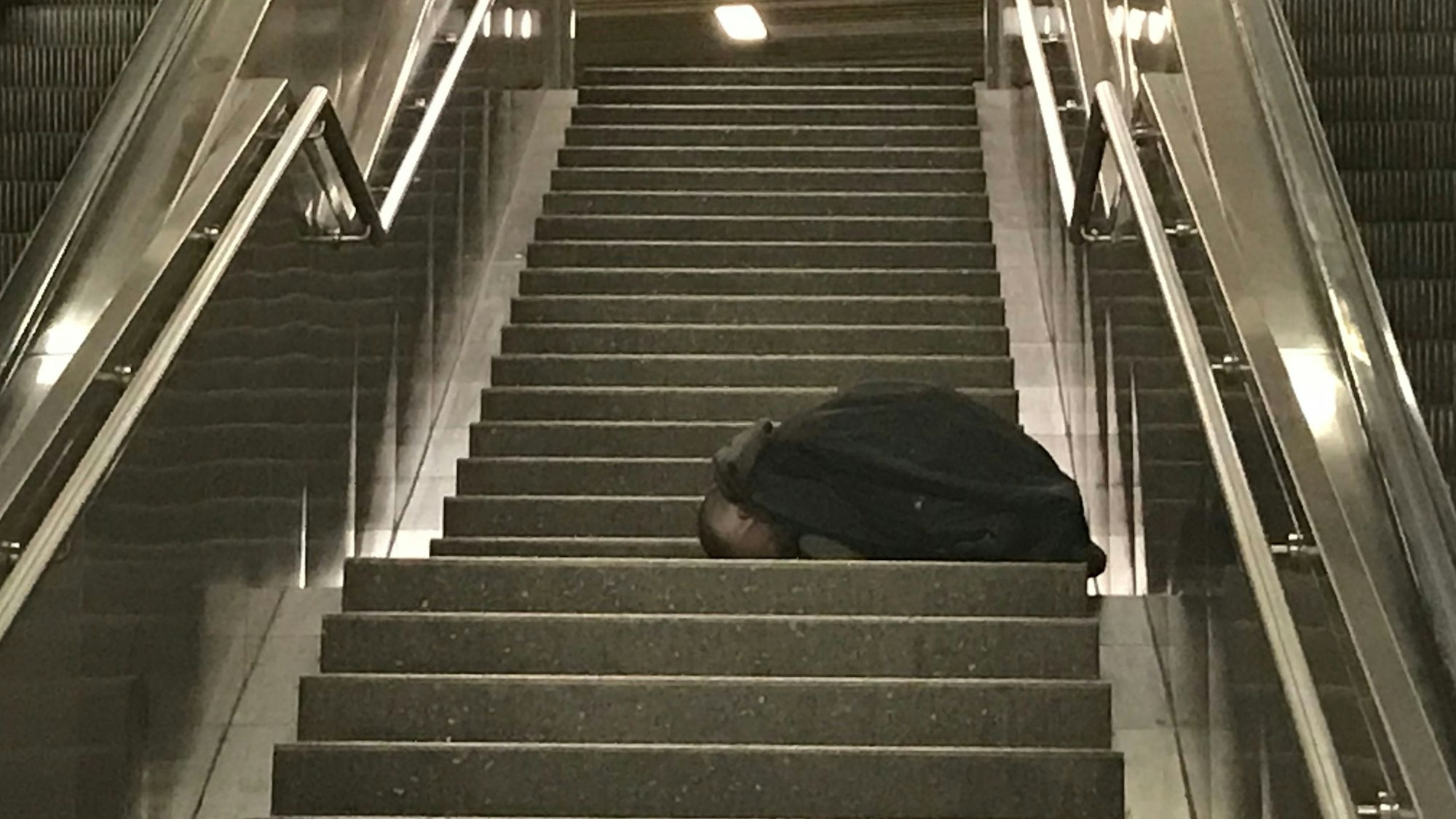 Eine Person sitzt zusammengesunken auf einem Treppenabsatz.