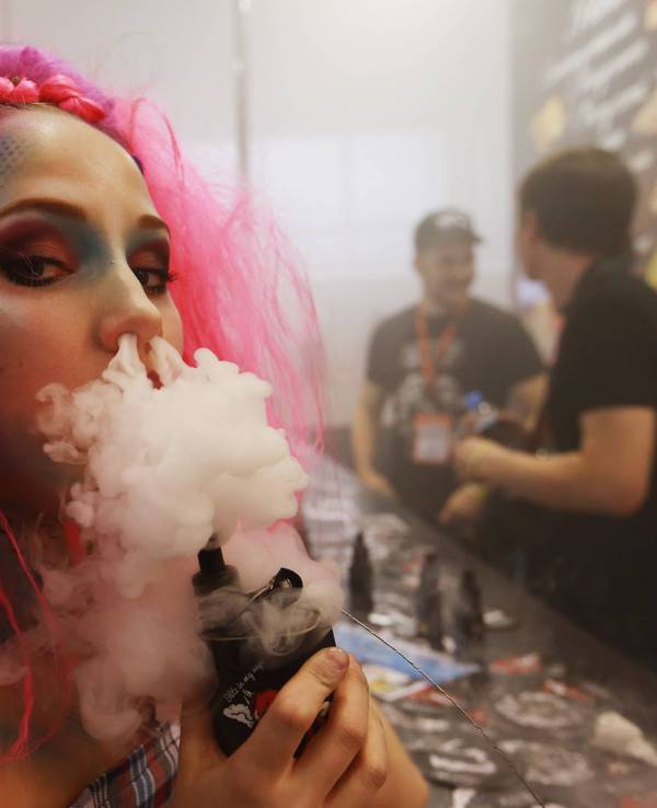 Junge Frau pustet Rauch aus einem Vape durch die Nase