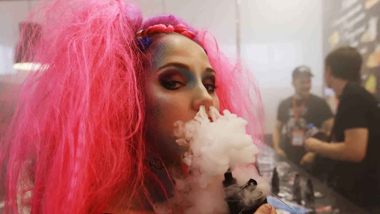 Junge Frau pustet Rauch aus einem Vape durch die Nase