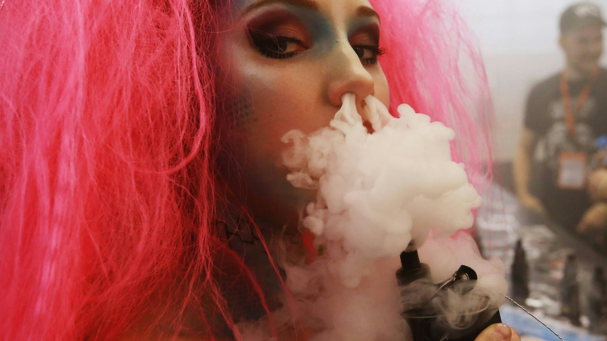 Junge Frau pustet Rauch aus einem Vape durch die Nase