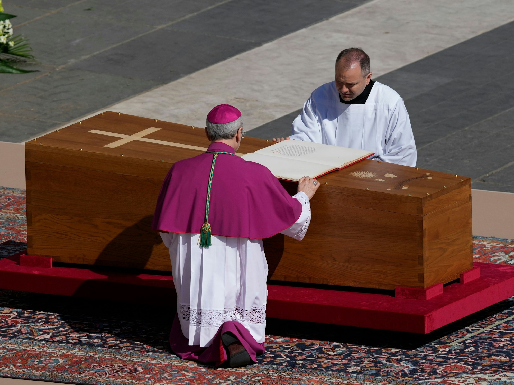 Erzbischof Diego Giovanni Ravelli, mit dem Rücken zur Kamera, kniet neben dem Sarg von Papst Franziskus auf dem Petersplatz im Vatikan.