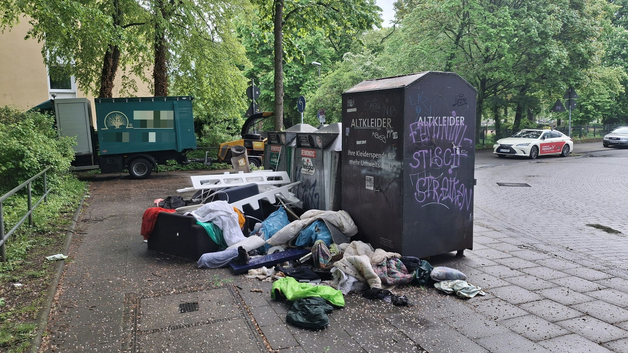 Kleidung und ein Sofa liegen vor einem Altkleidercontainer.