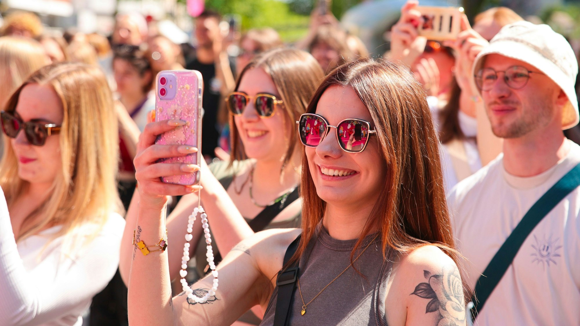Junge Menschen stehen bei einem Konzert beisammen, eine junge Frau filmt mit ihrem Handy.
