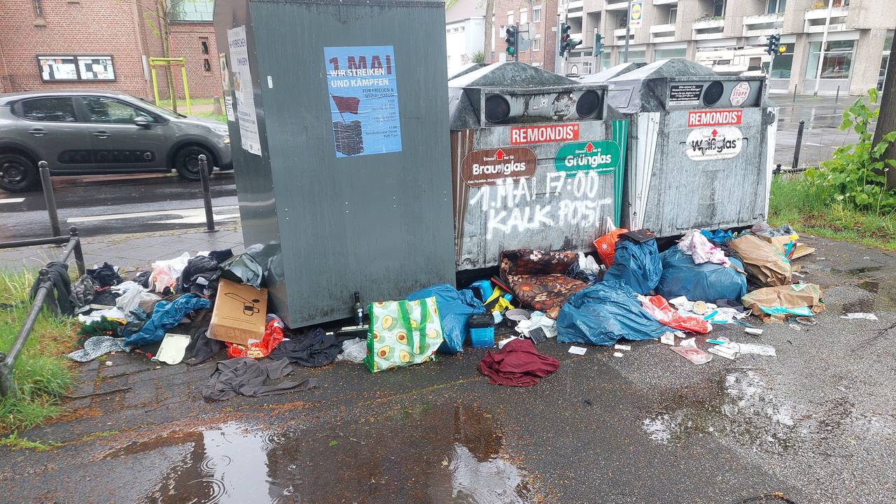 Vor und neben Altkleider- und Altglascontainern liegen volle Müllsäcke und Textilien wilddurcheinander.