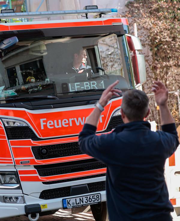 Ein Einsatzfahrzeug der Feuerwehr wird von einem Feuerwehrmann in einer engen Straße eingewiesen.