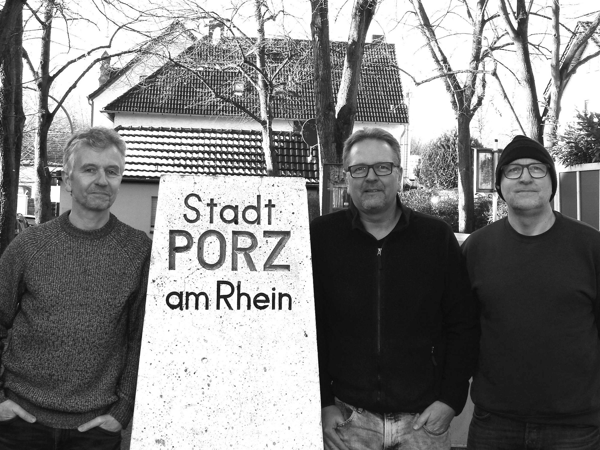 Drei Männer stehen neben einer Stele.