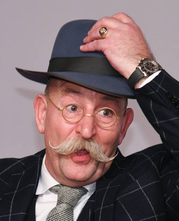 Horst Lichter, Fernsehkoch und Moderator, steht bei der Verleihung des Deutschen Fernsehpreises vor einer Wand und lüftet seinen Hut.