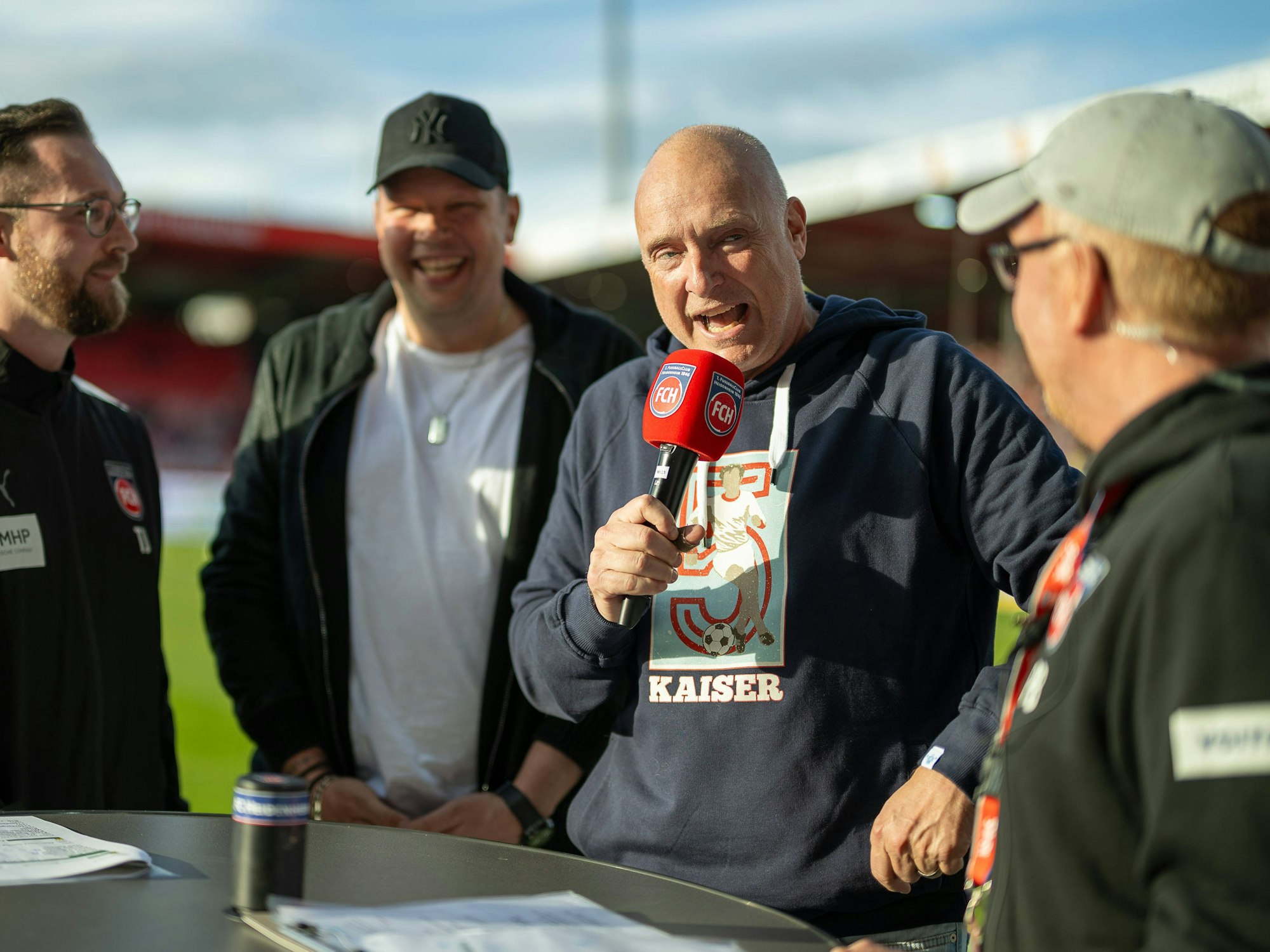Frank Buschmann spricht in ein Mikrophon, im Hintergrund lacht Wolff Fuss.