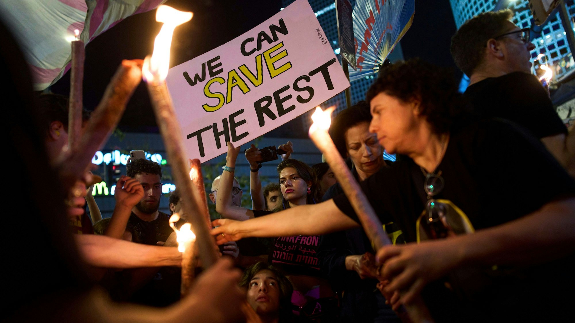 Demonstranten entzünden Fackeln während einer Demonstration, die die sofortige Freilassung der von der Hamas im Gazastreifen festgehaltenen Geiseln und ein Waffenstillstandsabkommen fordert. Eine Frau hält ein Schild mit der Aufschrift "We can safe the rest".