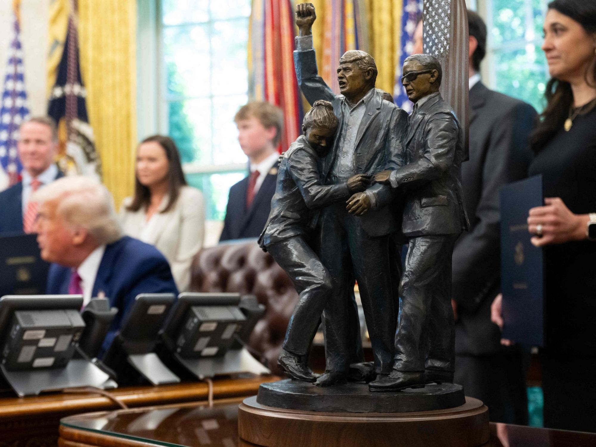 A statue depicting the attempted assassination of US President Donald Trump in Butler, Pennsylvania, sits alongside the Resolute Desk as Trump signs legislation relating to household consumer energy policies in the Oval Office of the White House in Washington, DC, on May 9, 2025. (Photo by SAUL LOEB / AFP)