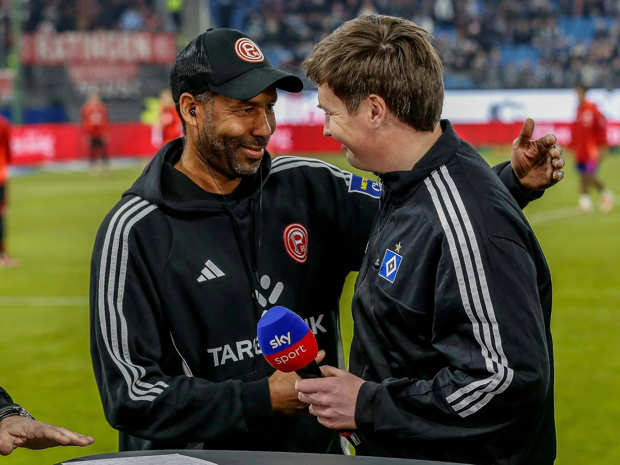 Merlin Polzin begrüßt seinen Freund und Kollegen Daniel Thioune bei einem TV-Interview am Spielfeldrand.