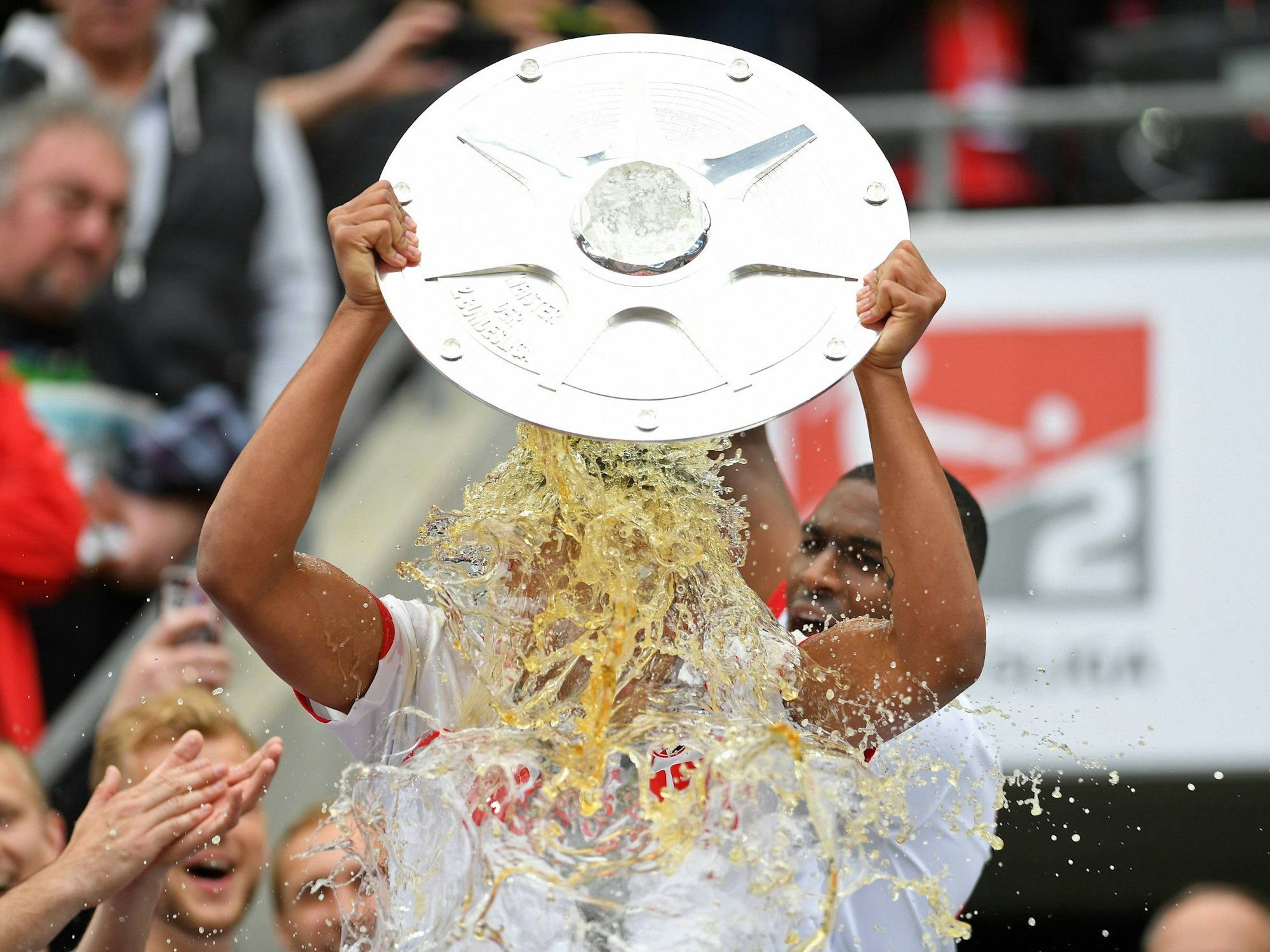 Nikolas Nartey hält die Schale hoch, während er von Anthony Modeste mit Bier übergossen wird.