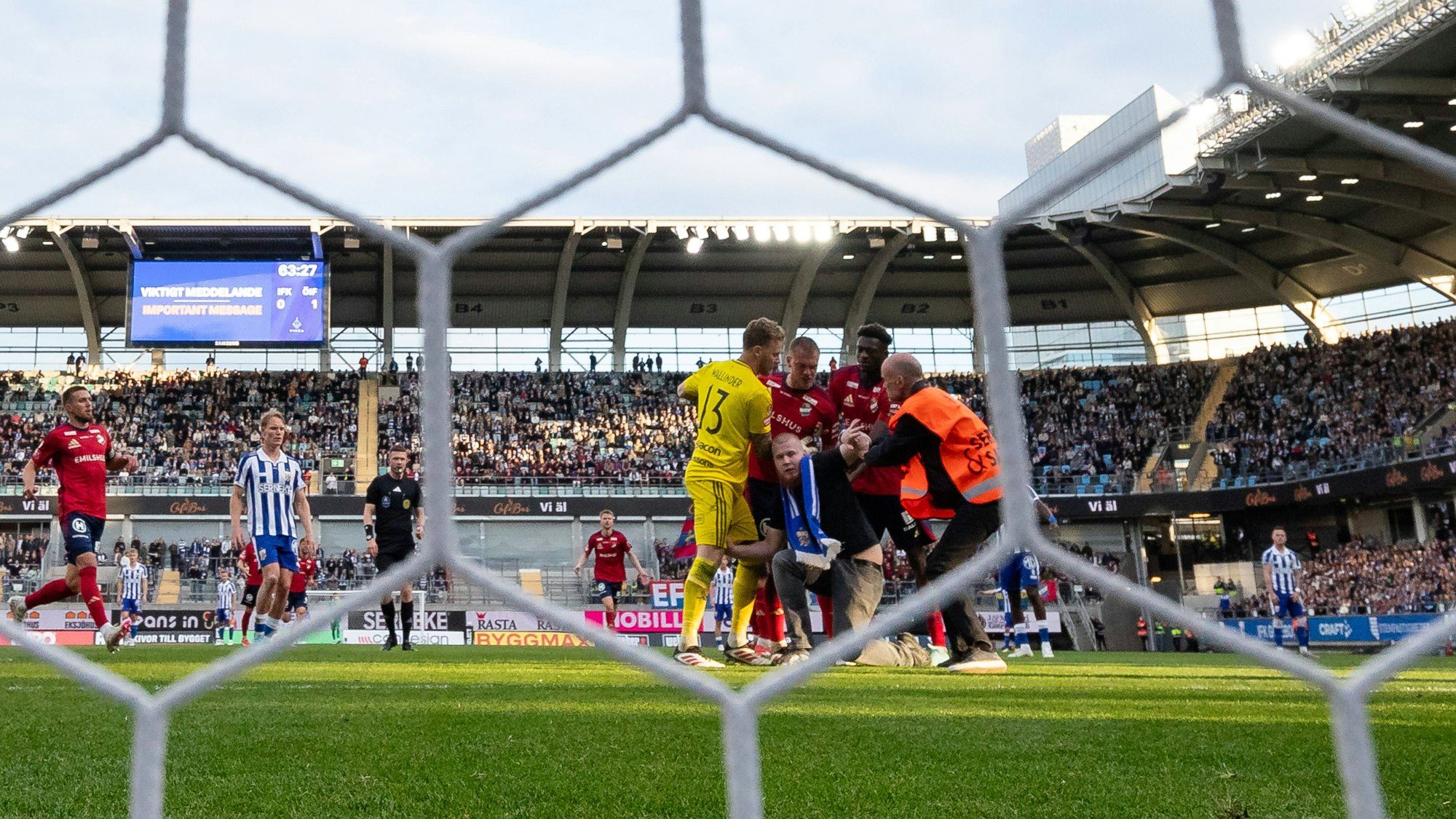 Ein Fan wird von Spielern und einem Ordner festgehalten, nachdem er einen Spieler auf dem Rasen angegriffen hat.