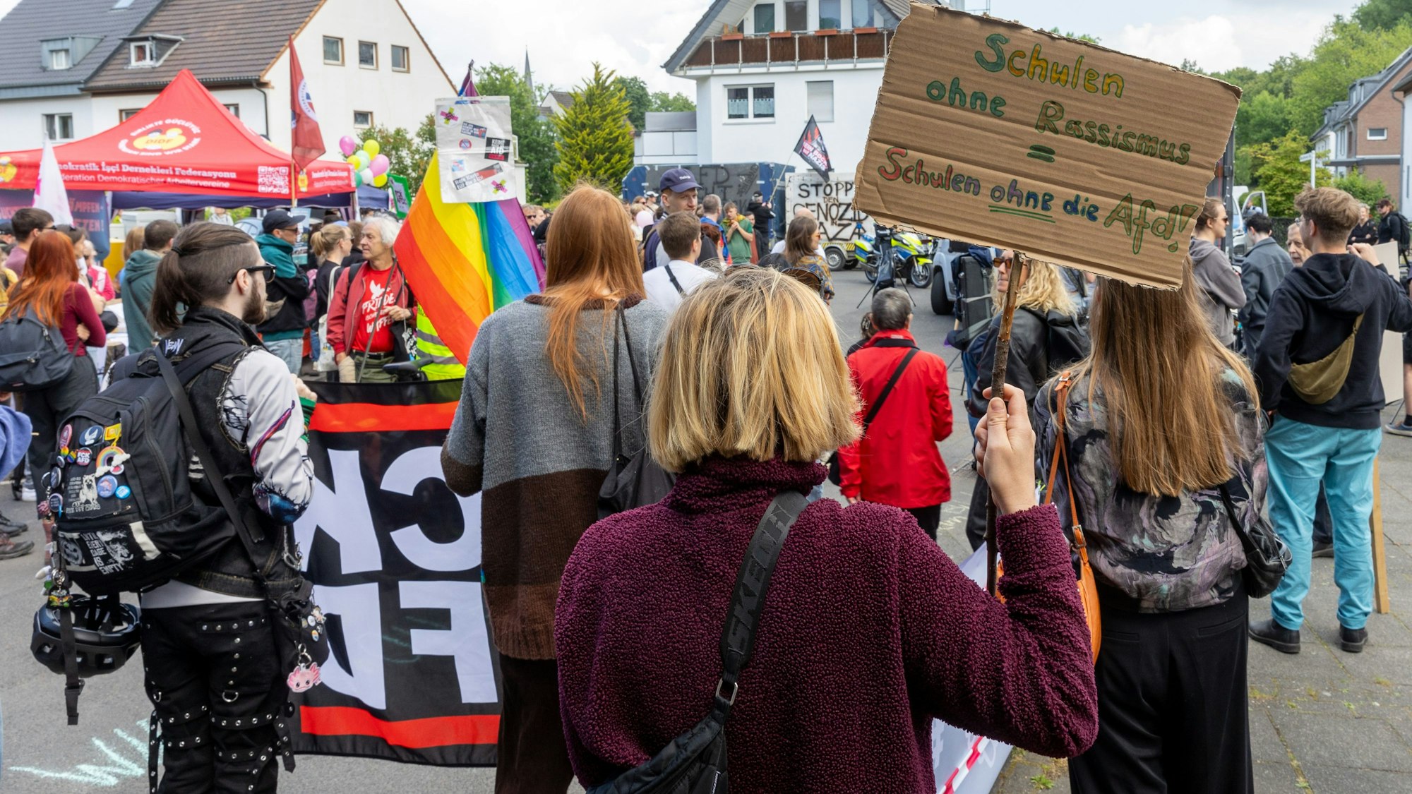 Menschen protestieren gegen eine AfD-Veranstaltung, eine Frau halt eine Pappe mit der Aufschrift „Schulen ohne Rassismus gleich schulen ohne die AfD“ hoch.