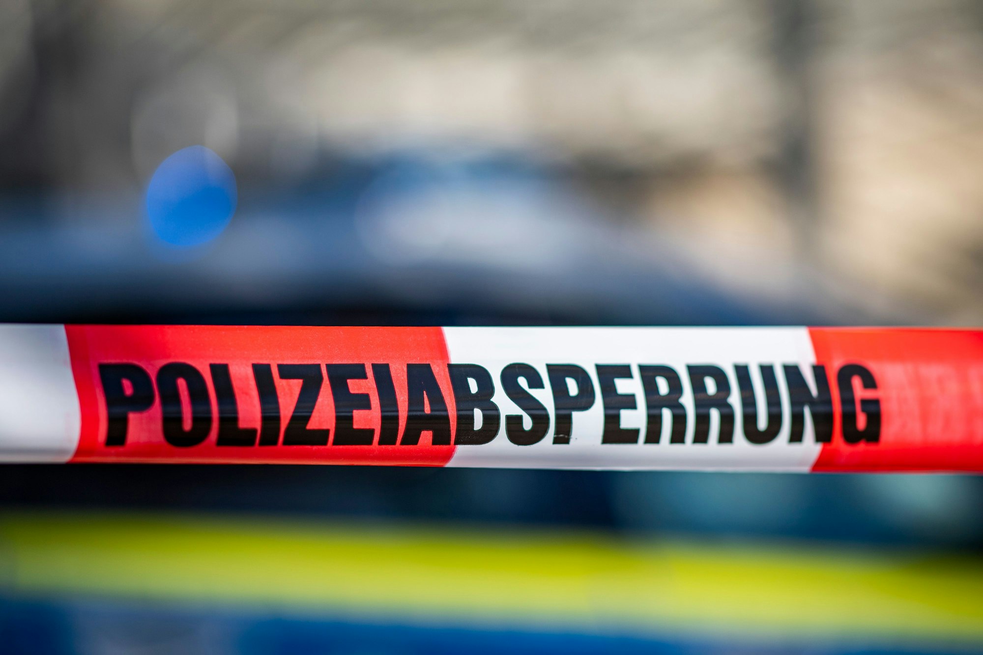 Ein Absperrband mit der Aufschrift „Polizeiabsperrung“ ist vor einem Polizeiwagen aufgespannt.