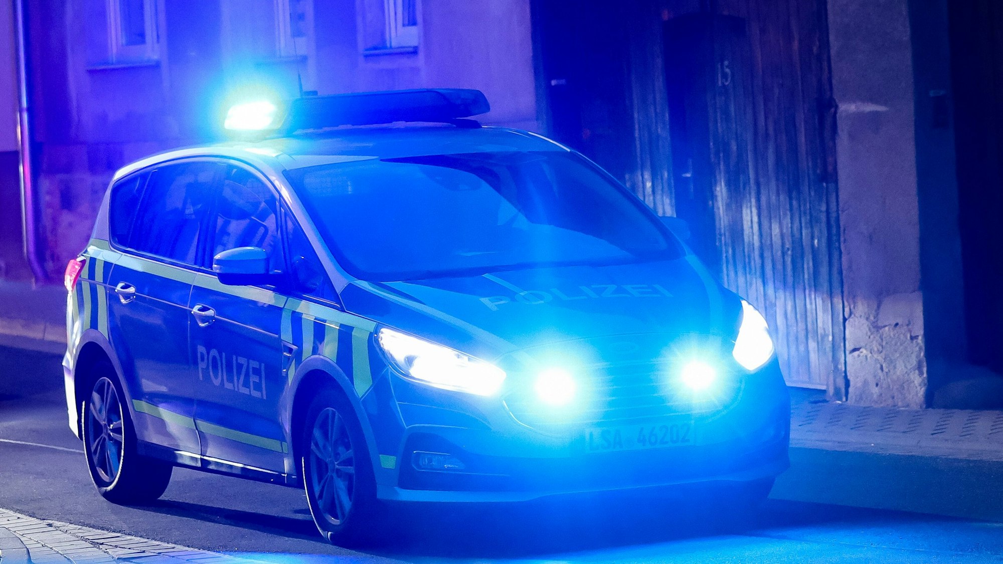 Ein Fahrzeug der Polizei fährt mit Blaulicht am Abend durch eine enge Straße.