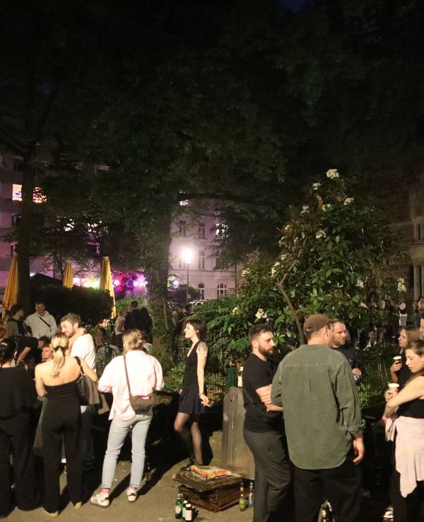 Auf einem Platz stehen in der Nacht junge Menschen in Gruppen, trinken Bier und unterhalten sich.