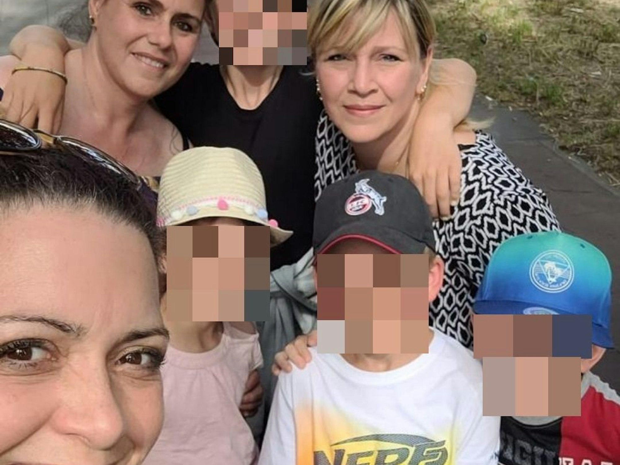 Ein Kind hat jeweils einen Arm um eine Frau gelegt, davor stehen drei weitere Kinder und eine weitere Frau.