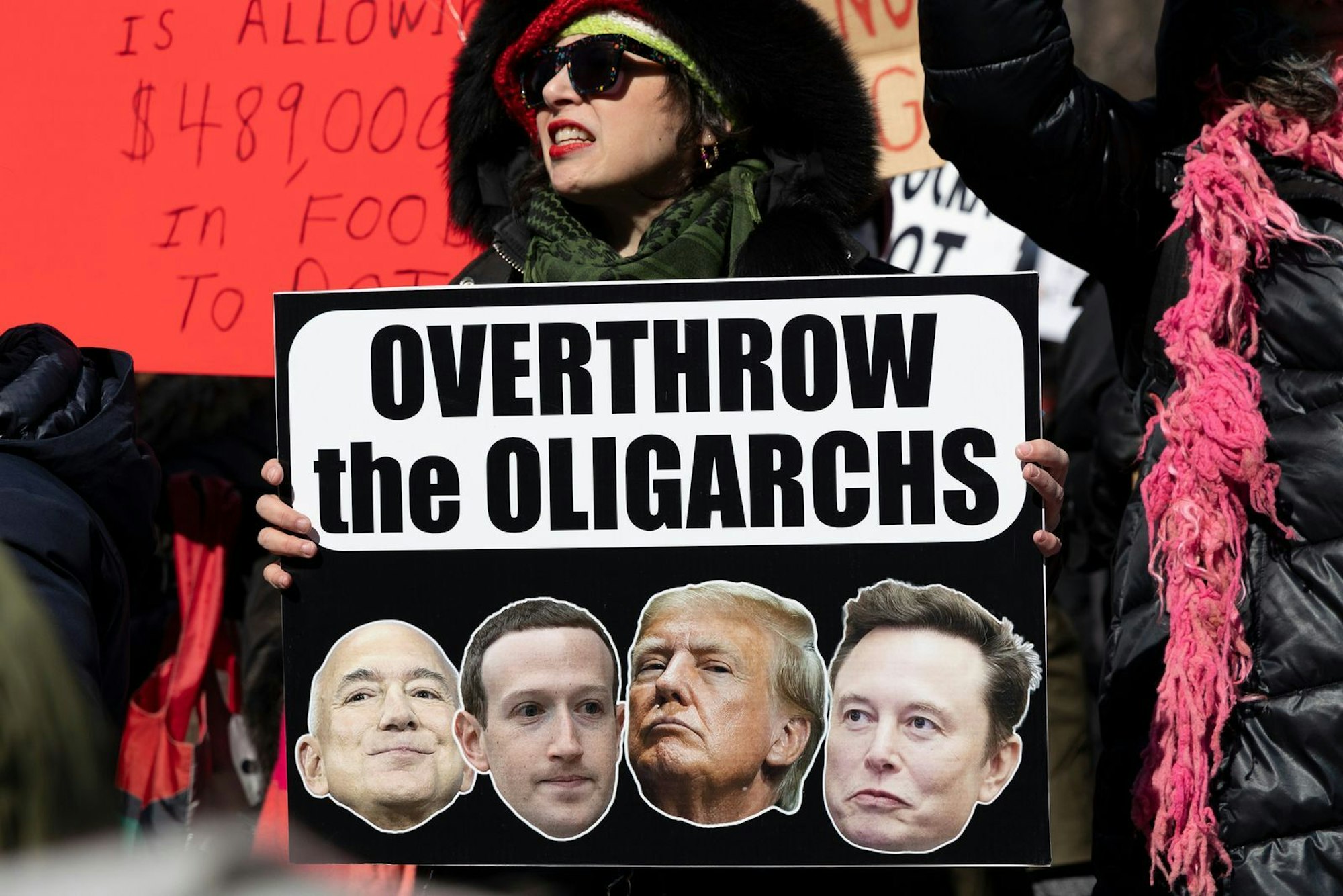 Es rumort in den USA. Diese Demonstrantin hält ein Schild mit der Aufschrift „Stürzt die Oligarchen“ in die Höhe. Das Plakat zeigt die Köpfe von Jeff Bezos (Amazon), Mark Zuckerberg (Facebook, Instagram, WhatsApp), Präsident Trump und Elon Musk (Tesla, X, Space X). (Bild: ZDF/Gina M Randazzo)