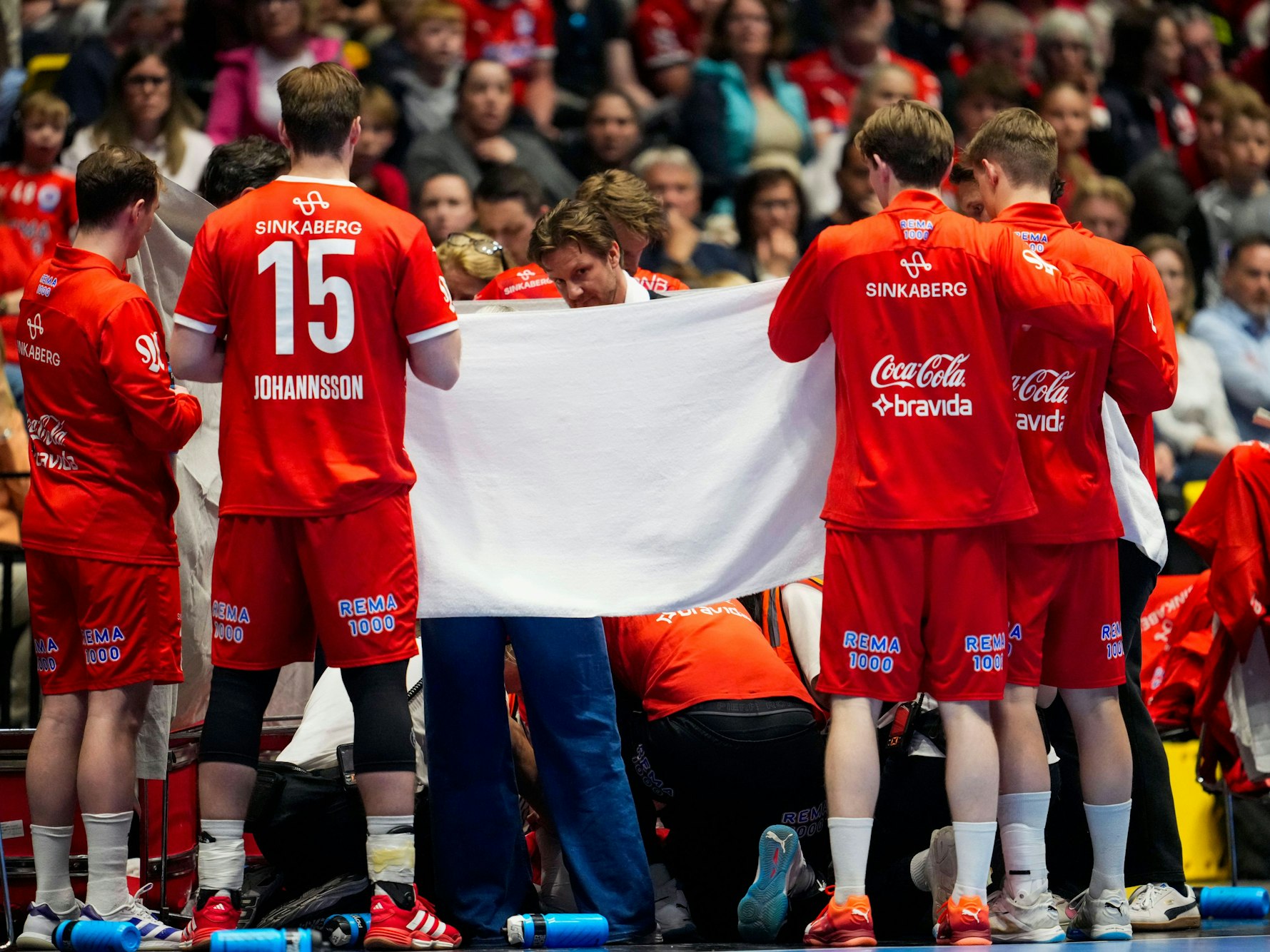 Nach dem Zusammenbruchs ihres Trainers schützen die Spieler ihn mit einem Sichtschutz vor neugierigen Blicken.