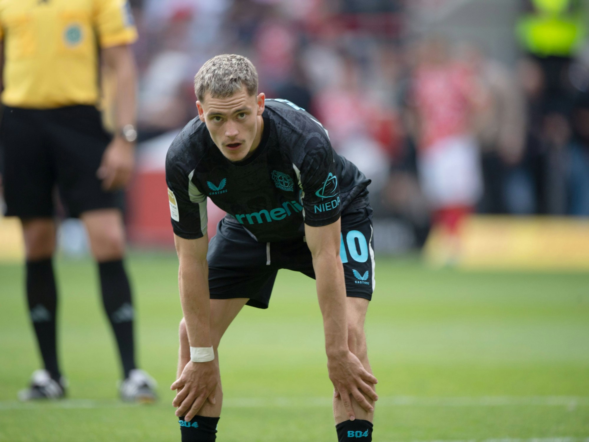 Florian Wirtz beugt sich nach vorne und stützt sich mit seinen Händen auf den Knien ab.