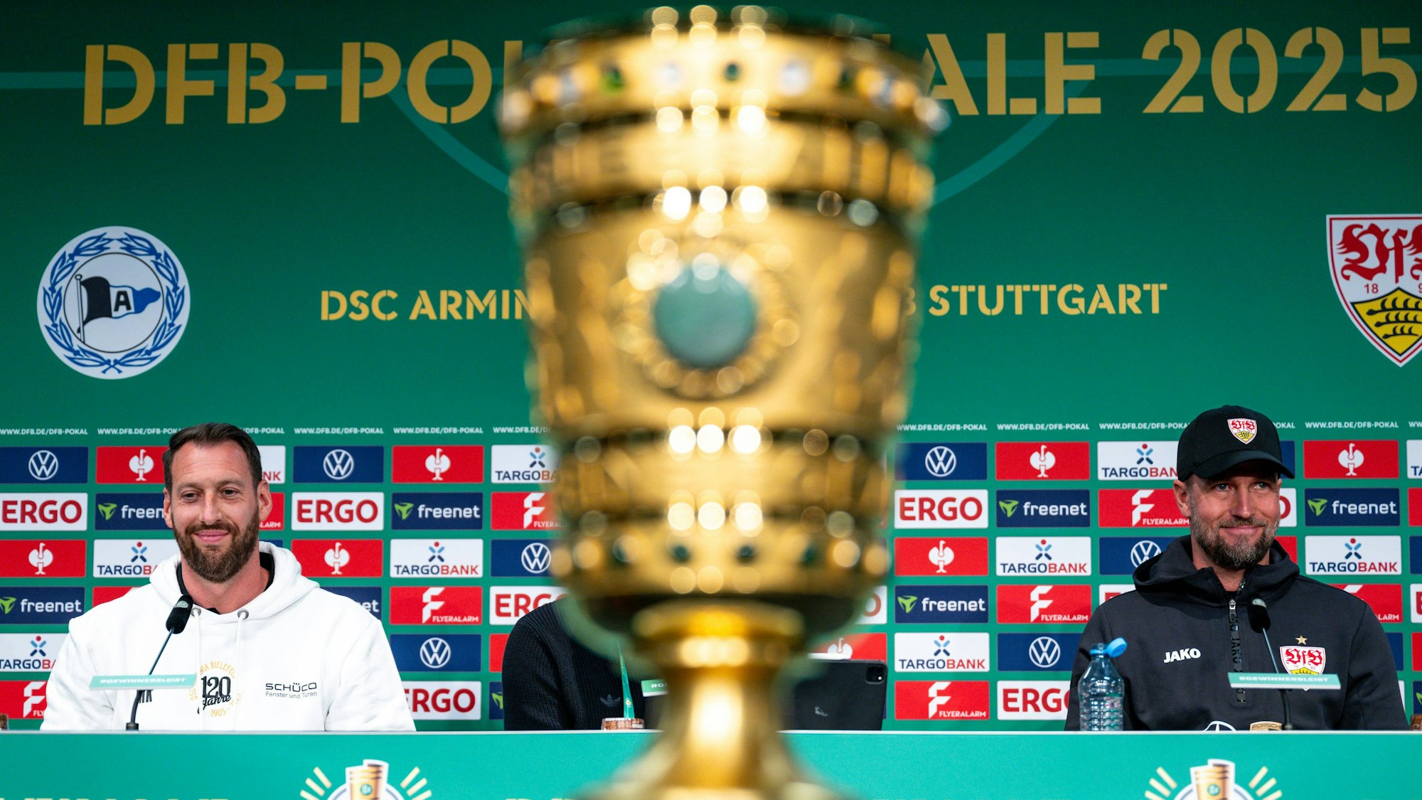 Mitsch Kniat und Sebastian Hoeneß sitzen bei einer Pressekonferenz, zwischen ihnen steht der DFB-Pokal.