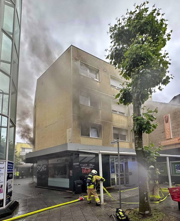 Feuerwehrleute stehen vor einem brennenden Haus.