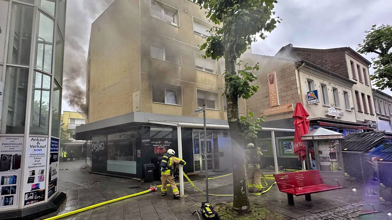 Feuerwehrleute stehen vor einem brennenden Haus.