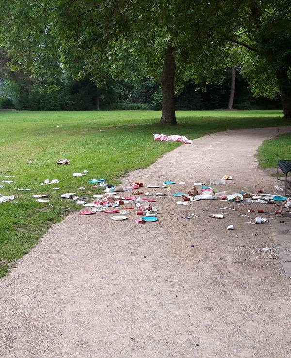 Abfall liegt vor einer Sitzbank in einem Park.