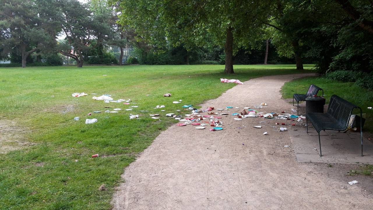 Abfall liegt vor einer Sitzbank in einem Park.