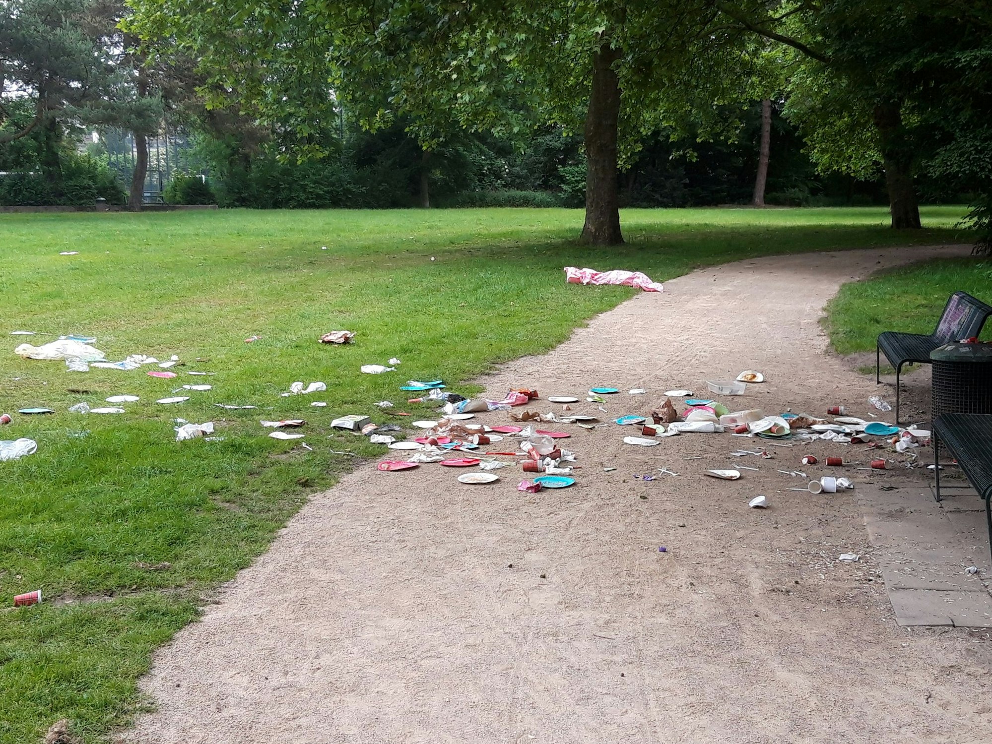 Abfall liegt vor einer Sitzbank in einem Park.