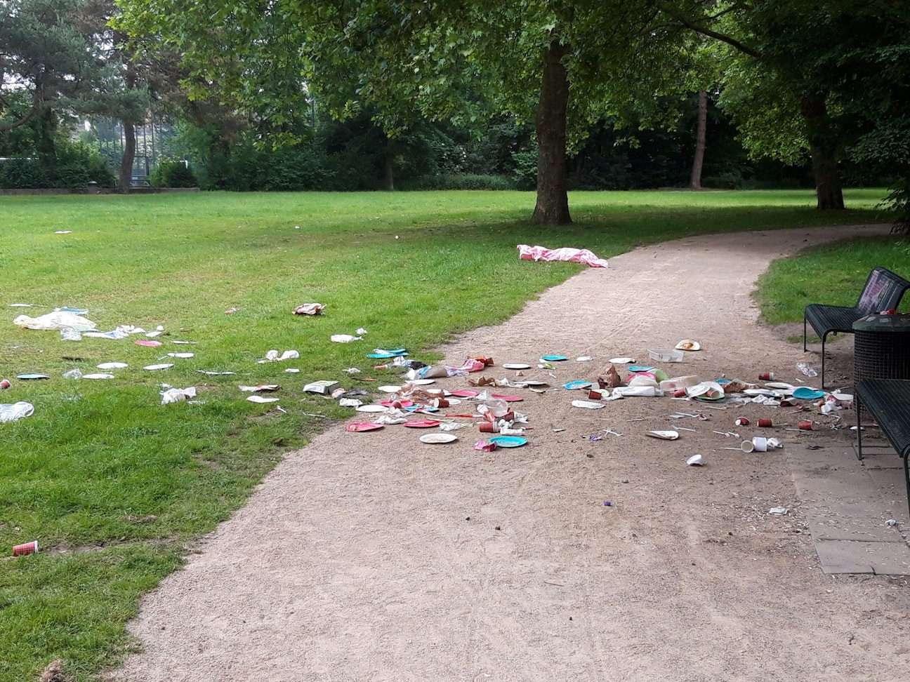 Abfall liegt vor einer Sitzbank in einem Park.