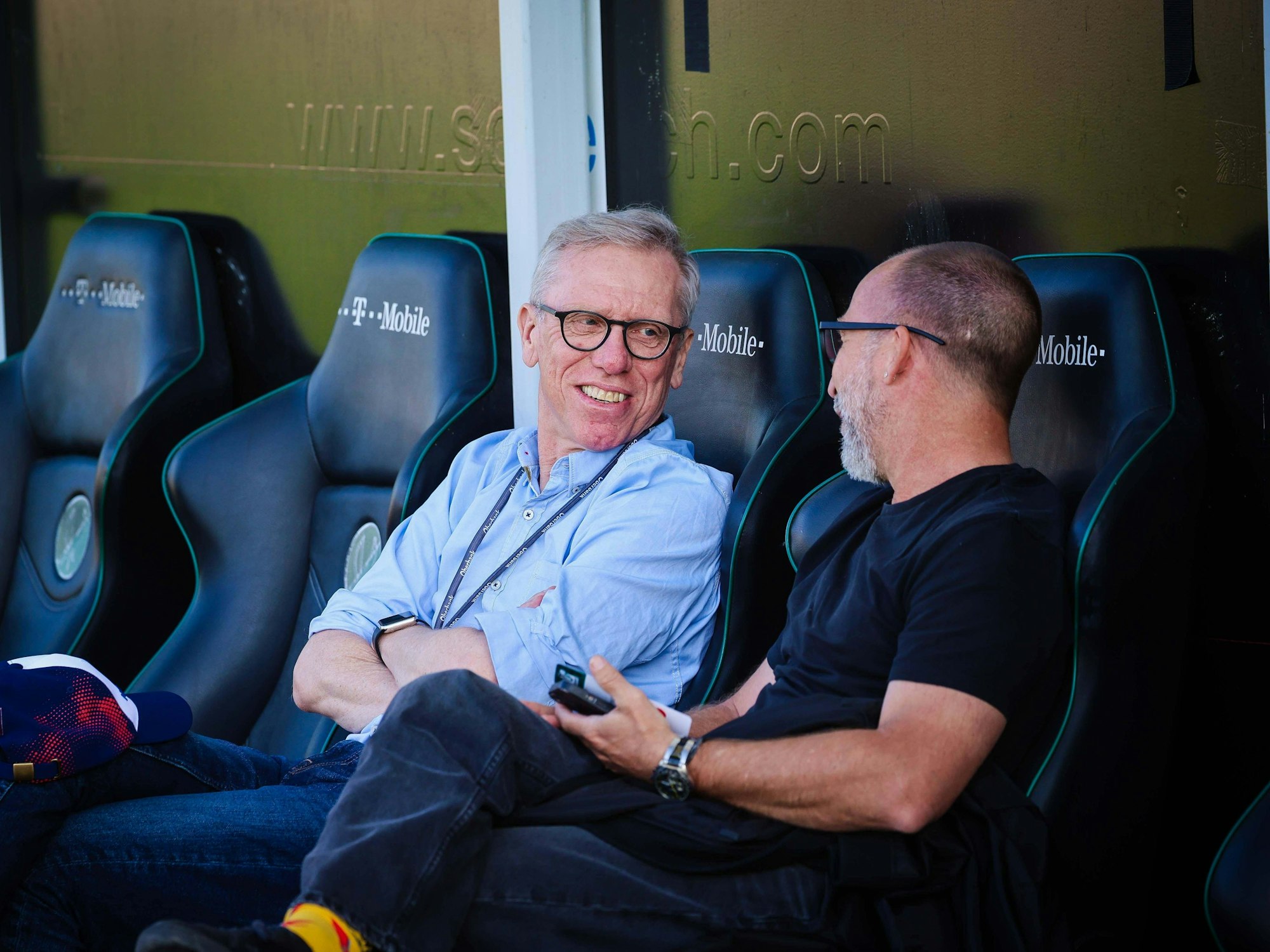 Peter Stöger sitzt auf der Trainerbank und unterhält sich.