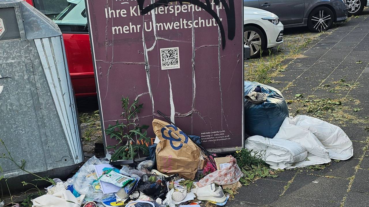 Abfall liegt neben Containern auf einem Gehweg.