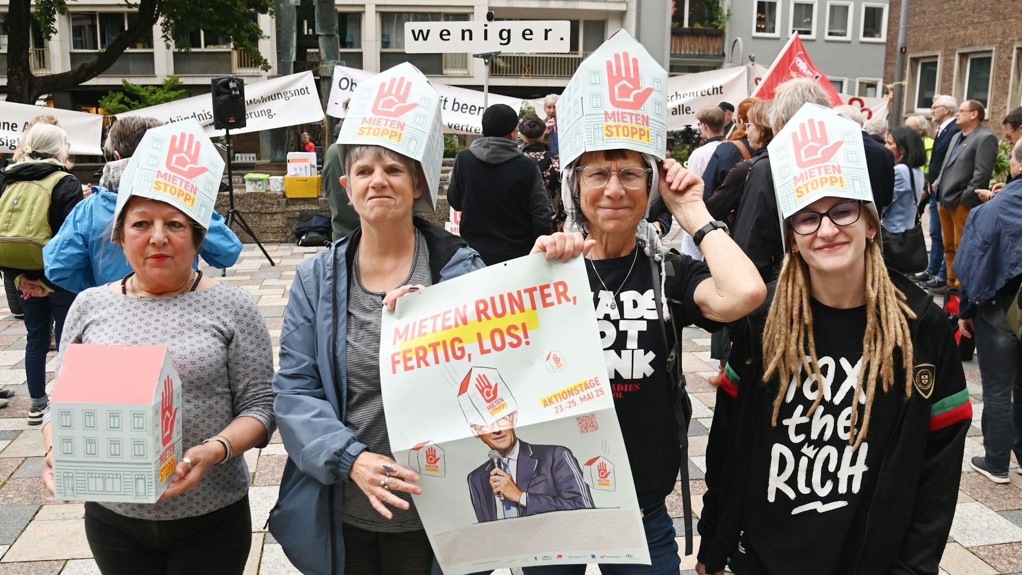 Vier Frauen tragen auf dem Kopf Papphüte mit der Aufschrift Mietenstopp, zwei halten zudem ein Plakat in Händen mit der Aufschrift „Mieten runter, fertig, los!“