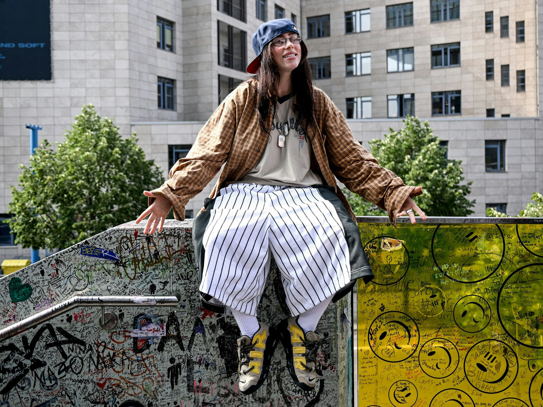 Die US-amerikanische Sängerin Billie Eilish sitzt auf einem Mauervorsprung.