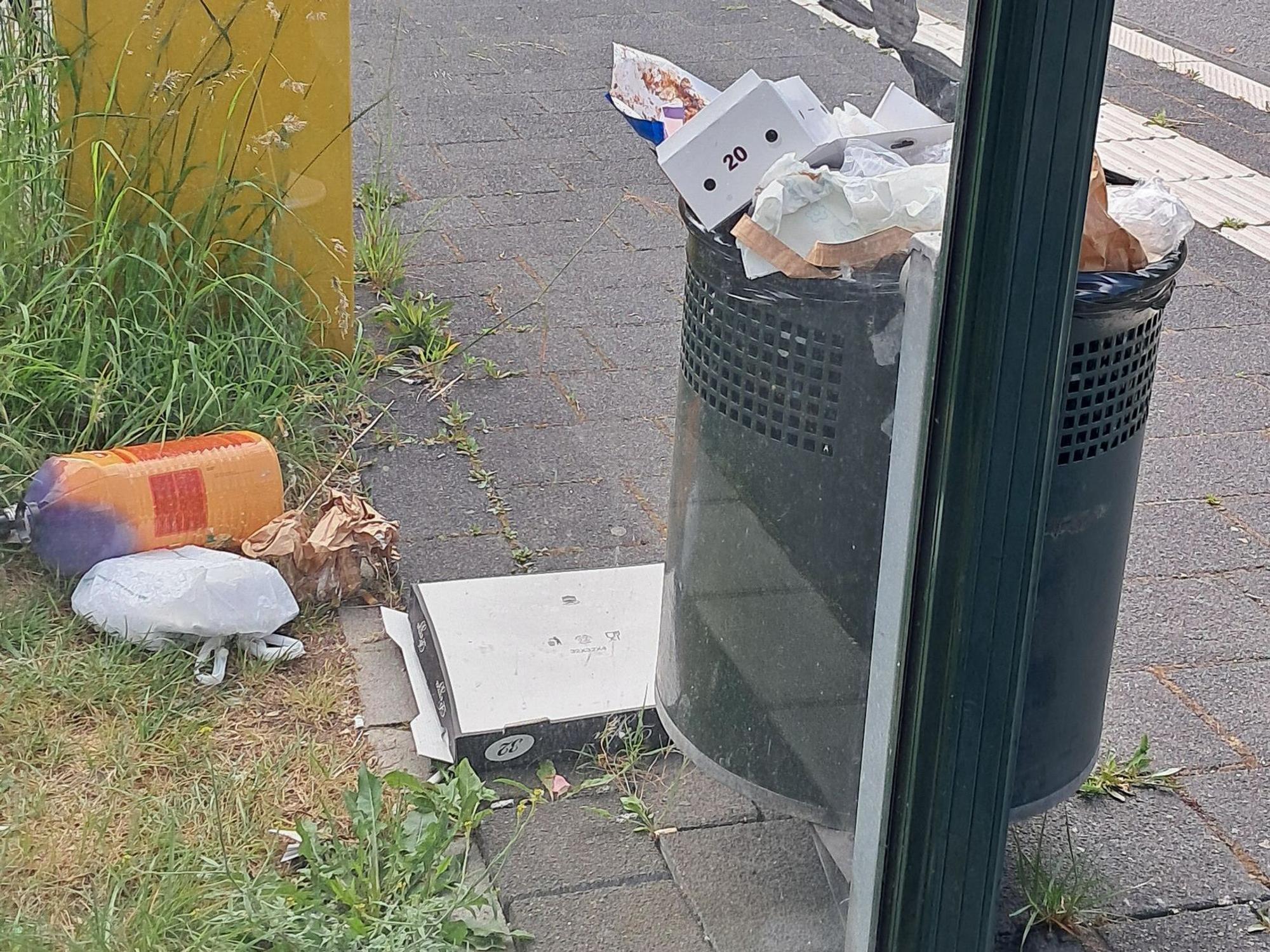 Neben einem vollen Mülleimer liegt Müll, unter anderem ein Pizzakarton, auf dem Boden.
