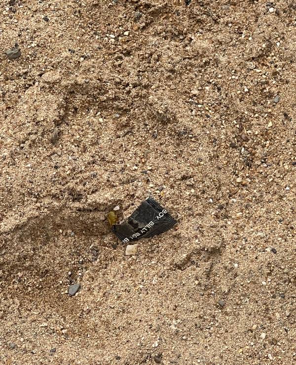 Eine aufgerissene Kondompackung liegt im Sand.