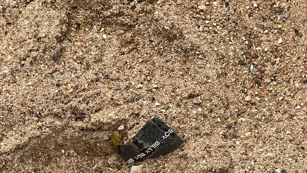 Eine aufgerissene Kondompackung liegt im Sand.