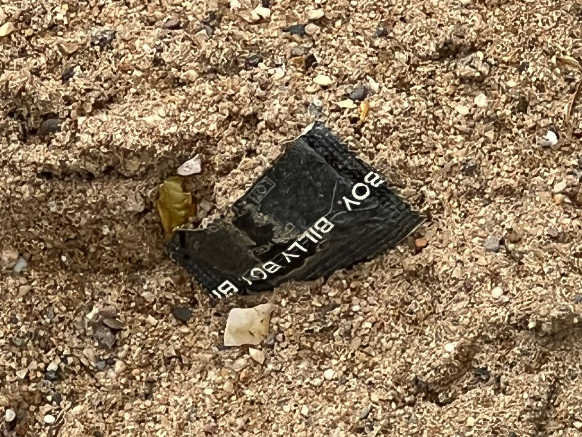 Eine aufgerissene Kondompackung liegt im Sand.