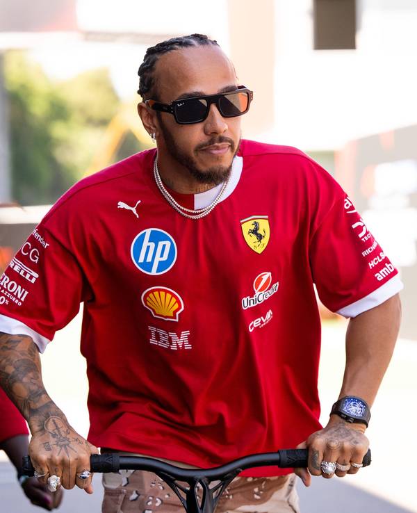 Lewis Hamilton fährt auf einem Roller, im Hintergrund sieht man seine Assistentin.