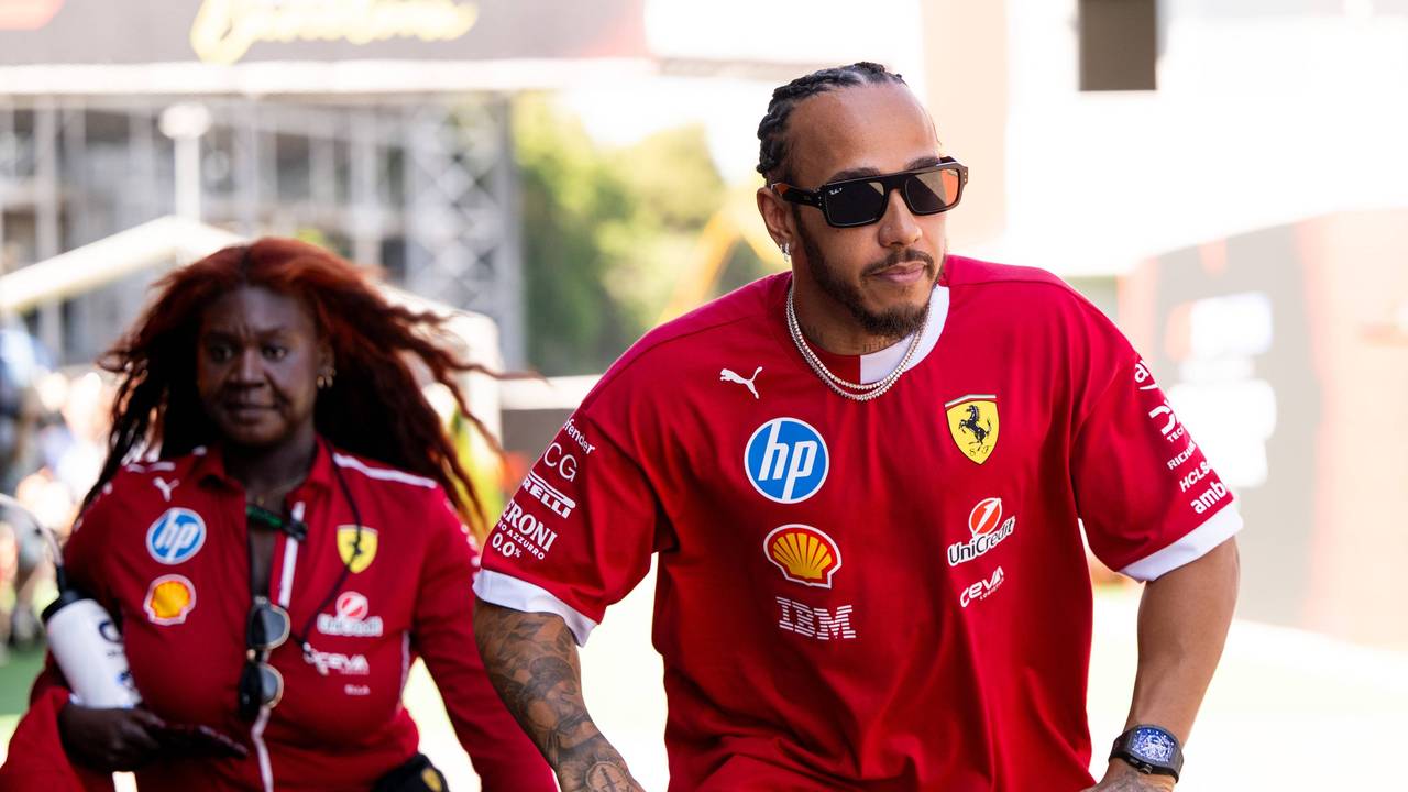 Lewis Hamilton fährt auf einem Roller, im Hintergrund sieht man seine Assistentin.